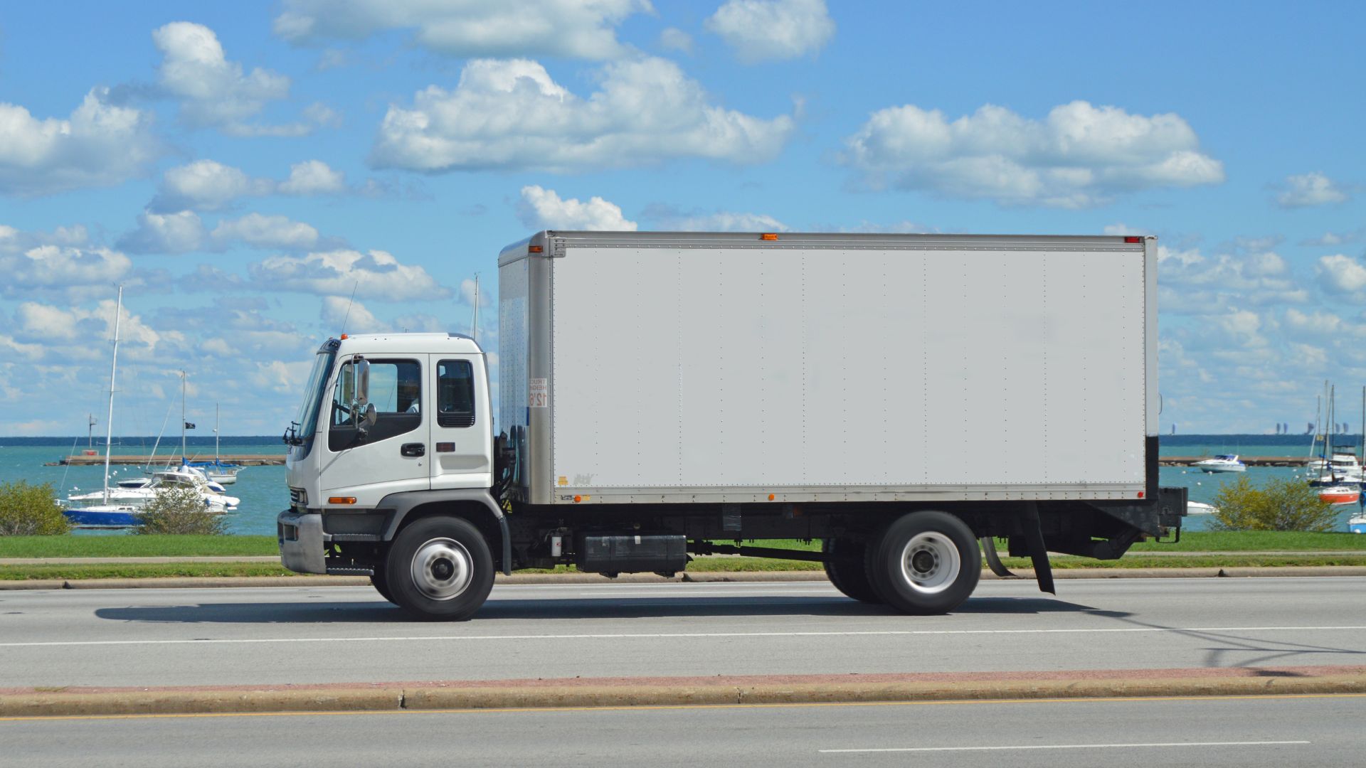 糸島から新鮮な牡蠣を運ぶ配送トラックが海辺の道を走る様子。青い海と空を背景に、毎朝直送される鮮度抜群の海の幸が奥糸に届けられます。