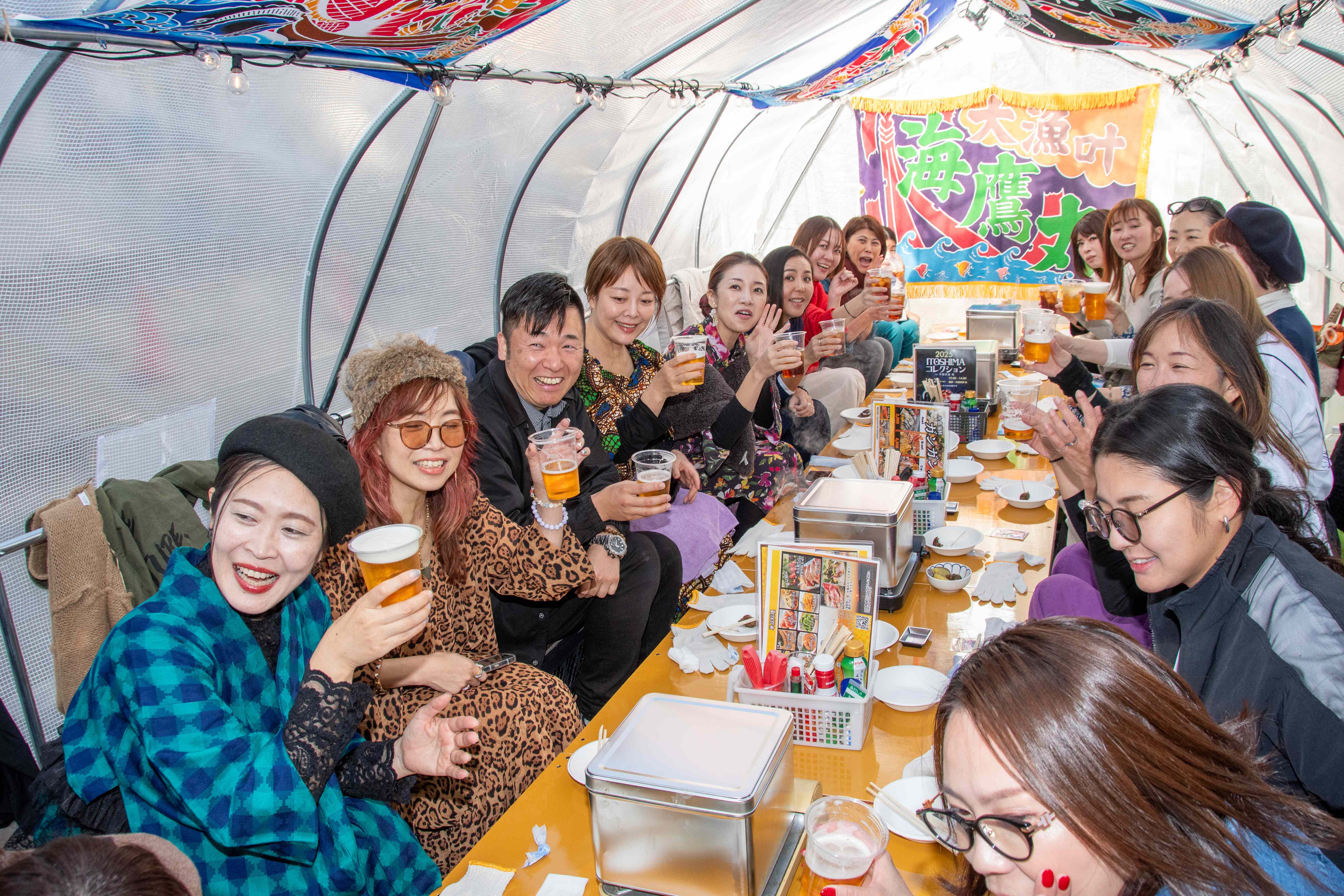 糸島の牡蠣小屋で楽しそうに乾杯するお客様たちの様子。笑顔あふれる団体利用風景。